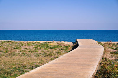 Footpath leading towards sea against clear sky