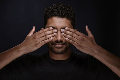 Close-up of young man covering eyes against black background