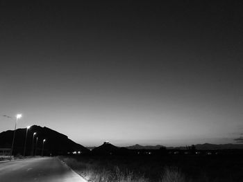 Road by silhouette city against clear sky at night