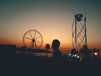 Side view of silhouette man looking at ferris wheel against sky during sunset