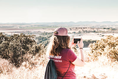 Rear view of woman photographing with mobile phone against sky