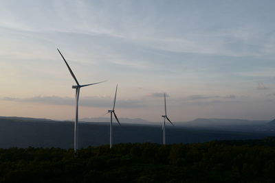 Wind turbines on field against sky during sunset