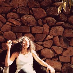 Portrait of young woman standing against stone wall