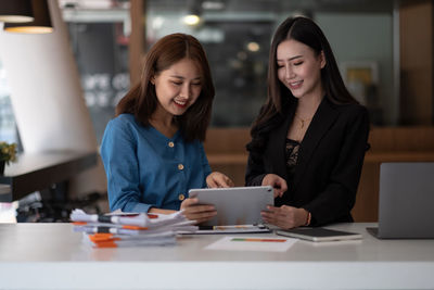 Portrait of smiling young woman using mobile phone while sitting in cafe