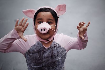 Boy wearing pig costume looking away while gesturing against wall