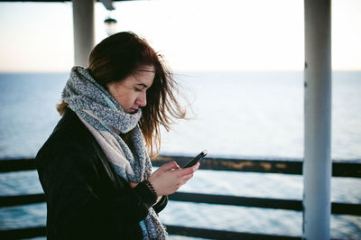 Side view of young woman using phone on pier over sea