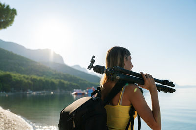 Rear view of woman standing by lake against sky