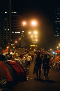 People on illuminated city against sky at night