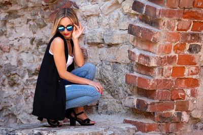 Full length of woman sitting against brick wall