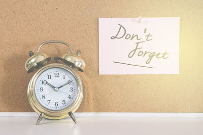 Close-up of alarm clock by paper with text on wall