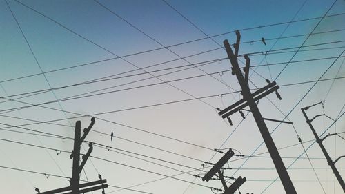 Low angle view of silhouette electricity pylons against clear sky