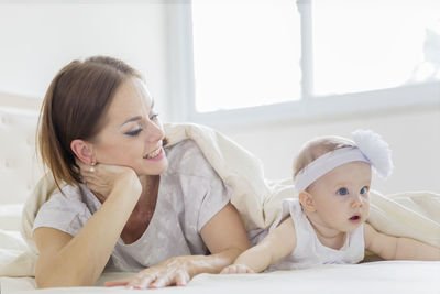 Portrait of mother and daughter lying on bed under blanket