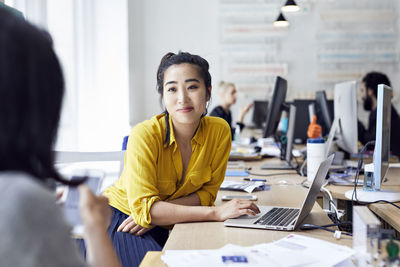 Businesswoman looking at female colleague with coworkers sitting in background