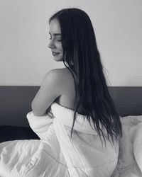Young woman looking away while sitting on bed