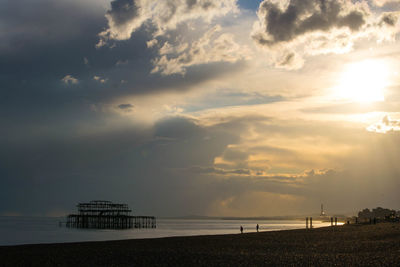 West pier in sea against cloudy sky during sunset