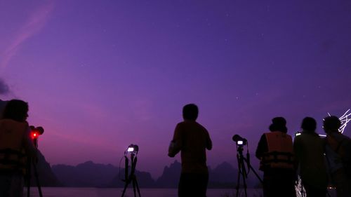 Rear view of silhouette people photographing against sky at night