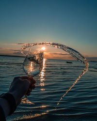 Person holding illuminated lighting equipment against sea during sunset