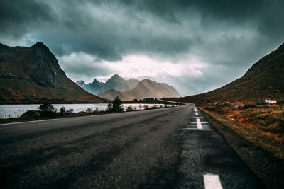 Road leading towards mountains against cloudy sky