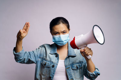 Close-up of young woman wearing flu mask holding megaphone against white background