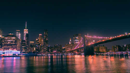 Illuminated bridge over river against buildings at night