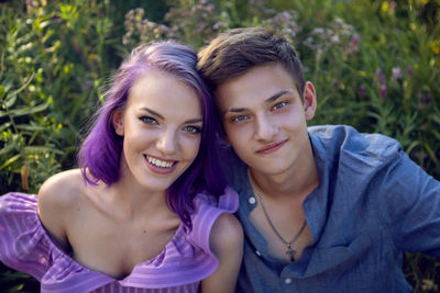 Lovers are a beautiful guy with a girl with purple hair and bouquet of flowers sitting on the grass