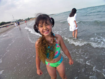 Portrait of cute smiling girl in swimwear at beach against sky