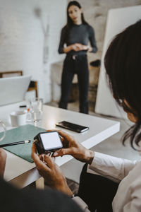 Midsection of woman holding mobile phone while standing on table