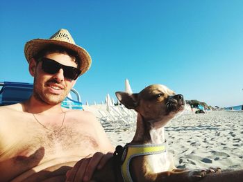 Portrait of shirtless young man relaxing with dog at beach