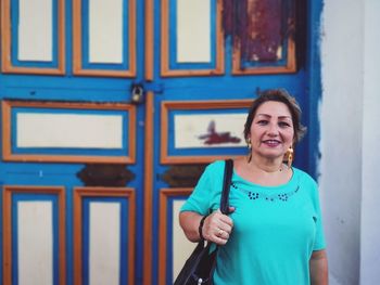 Portrait of smiling woman standing against blue door