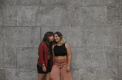 Portrait of two girls standing against stone wall