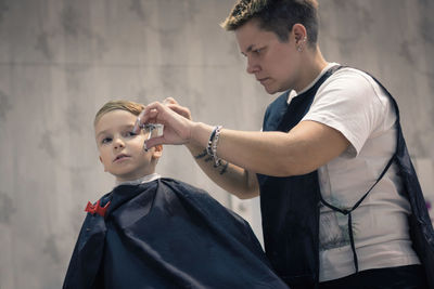 Side view of barber cutting boy hair in salon