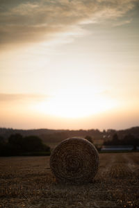 Hay bales on field against sky during sunset