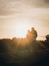 Rear view of silhouette couple standing against sky during sunset