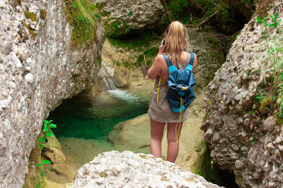 Rear view of woman standing by stream amidst rocks in forest