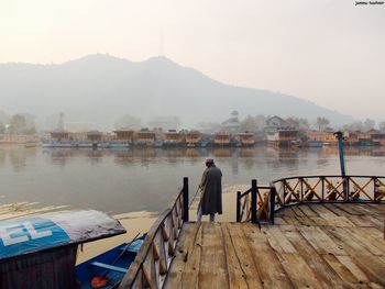 Rear view of man on pier by lake against sky