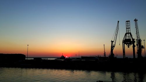 Silhouette sailboats moored at harbor against clear sky during sunset