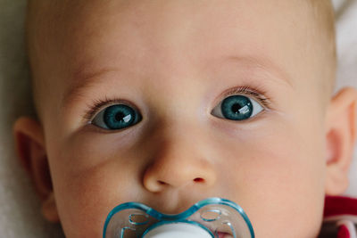 Close-up portrait of cute baby boy sucking pacifier on bed