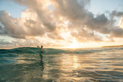 Shirtless man fishing in sea against sky during sunset