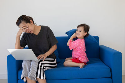 Full length of woman using mobile phone while sitting on sofa