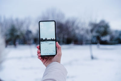 Unrecognizable woman hand taking picture with mobile phone to snowy landscape during winter season.