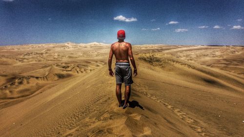 Rear view of shirtless man standing on sand dune at desert