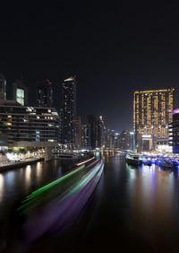 Illuminated buildings by river against sky in city at night