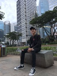 Full length of man sitting against modern buildings in city