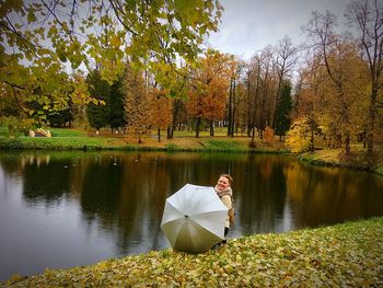 Woman with umbrella by lake at park during autumn
