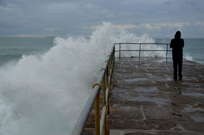 Rear view of man standing on railing against power of the sea