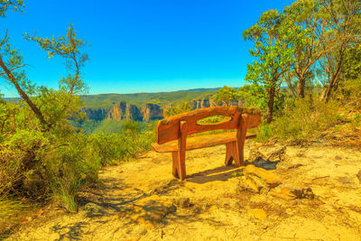 Empty bench by trees on landscape against blue sky