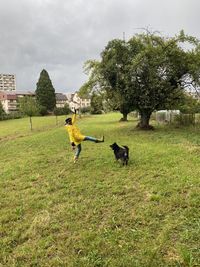 Full length of woman playing with dog on field against sky