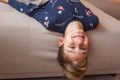 Portrait of happy boy lying upside down on sofa