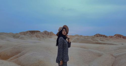 Portrait of young woman standing on desert against sky