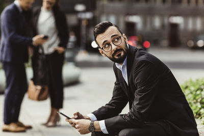 Businessman looking up while using mobile phone outdoors